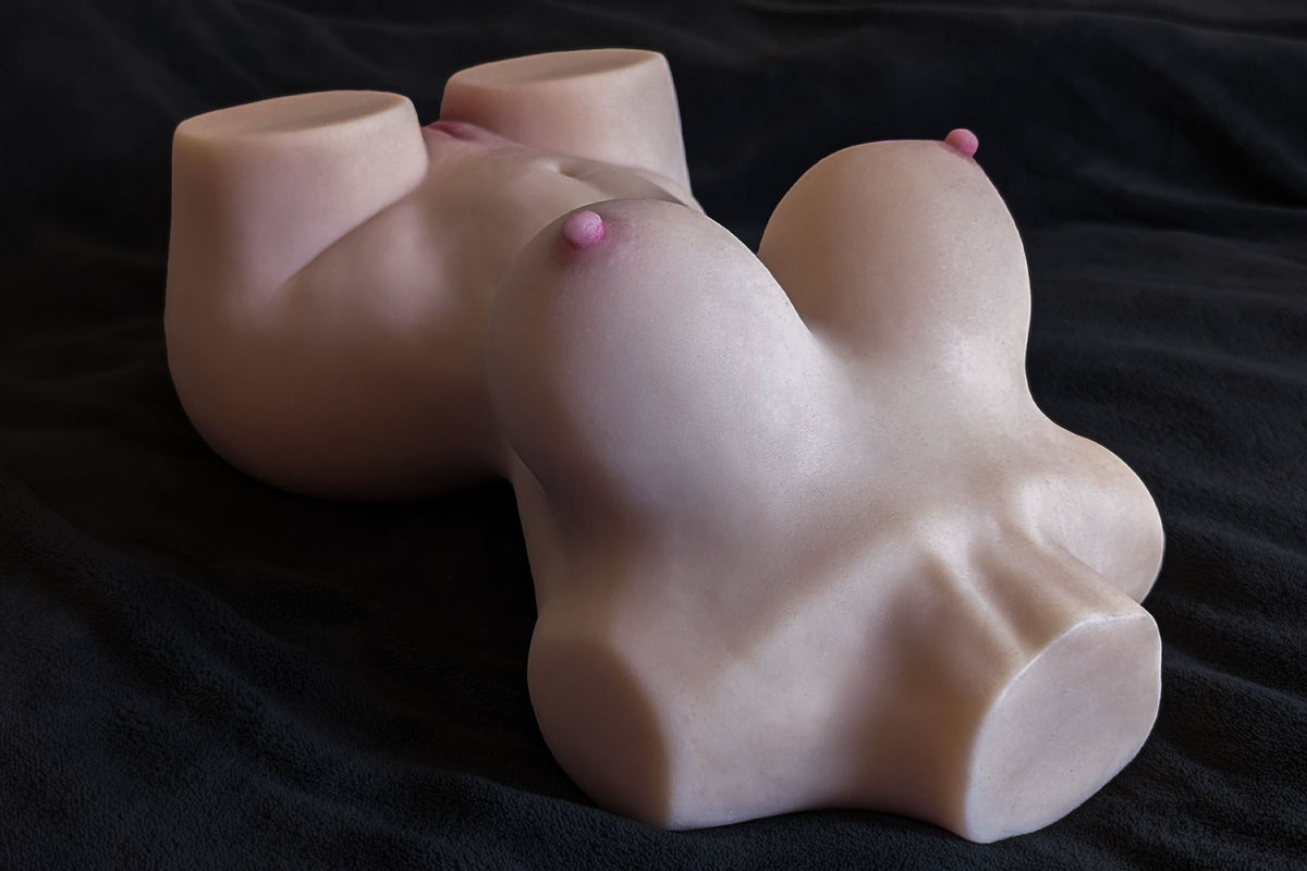 Sex doll torso Sara lying on a dark surface, side view with breasts